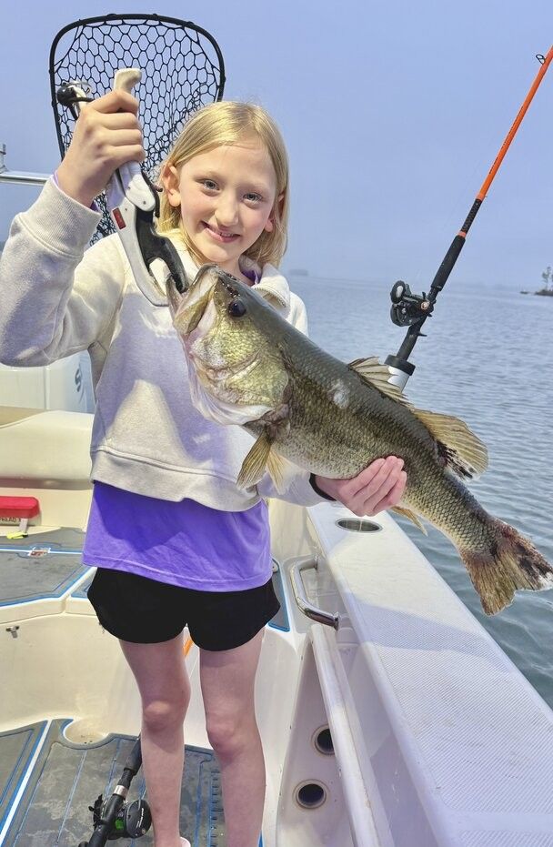 Freshly caught bass being held up on fishing boat deck with net and fishing rod visible
