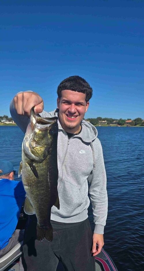 Angler holding freshly caught bass on boat deck with clear blue water and shoreline in background