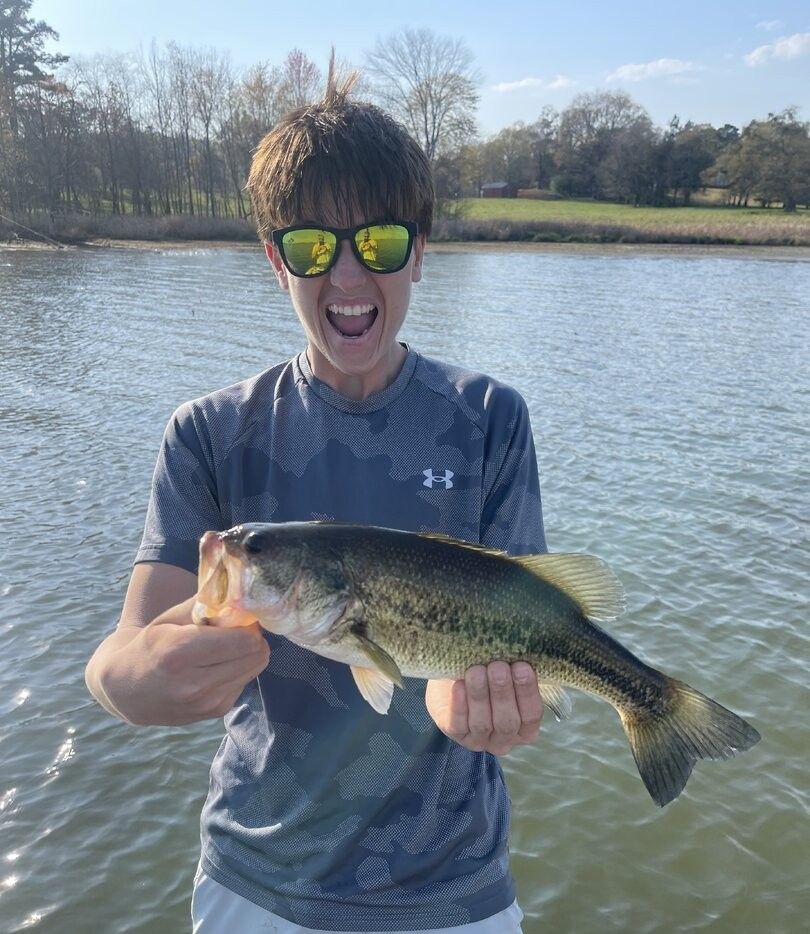 Angler holding caught bass fish on lake with trees in background