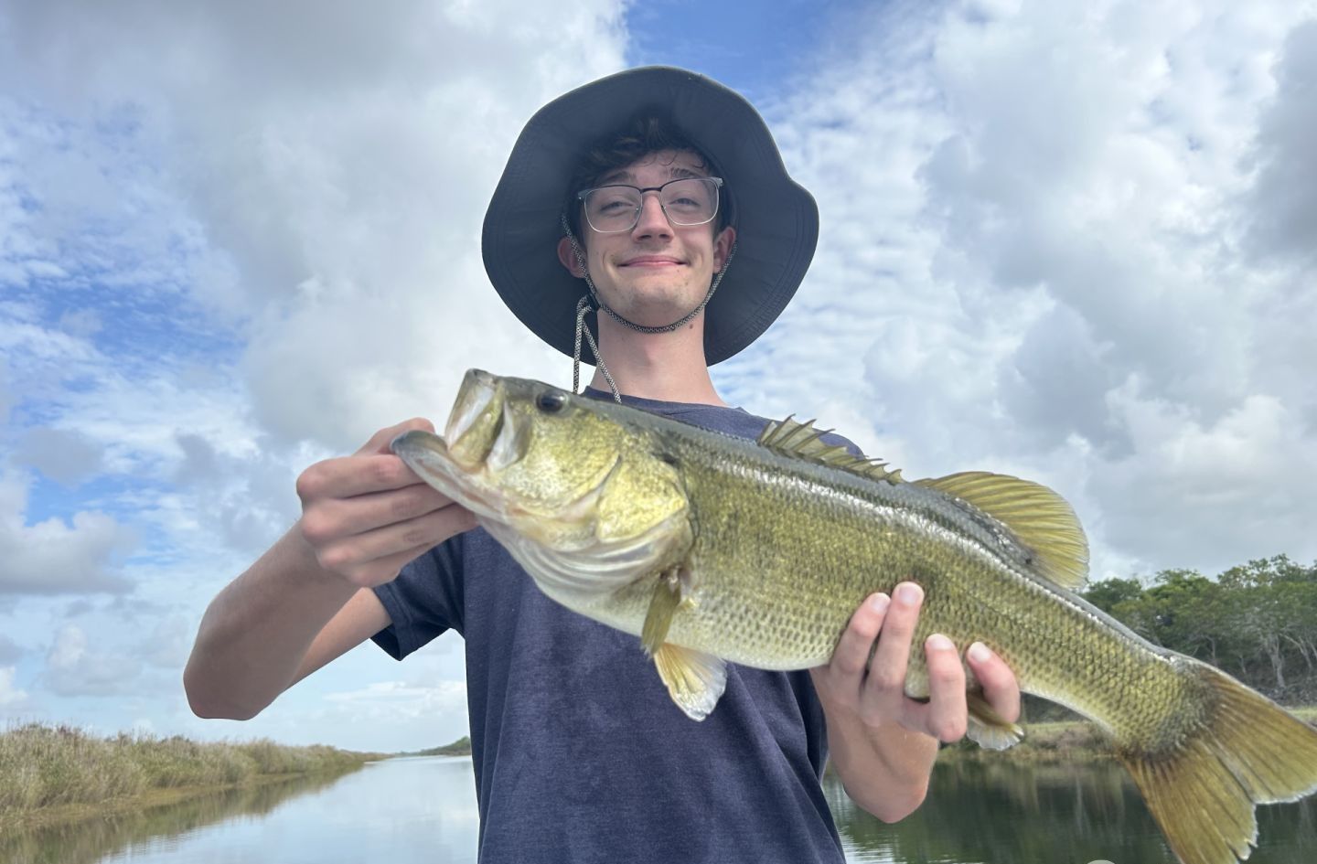Angler holding freshly caught bass fish outdoors near water