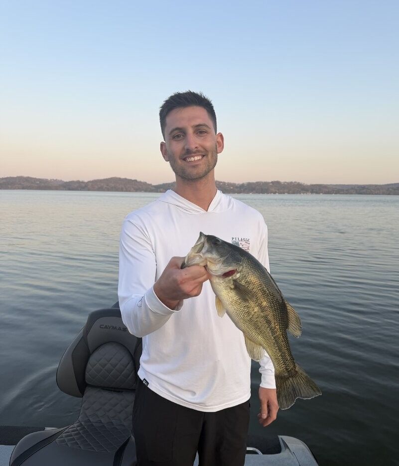 Freshly caught bass being held up on a boat during a fishing trip on a calm lake