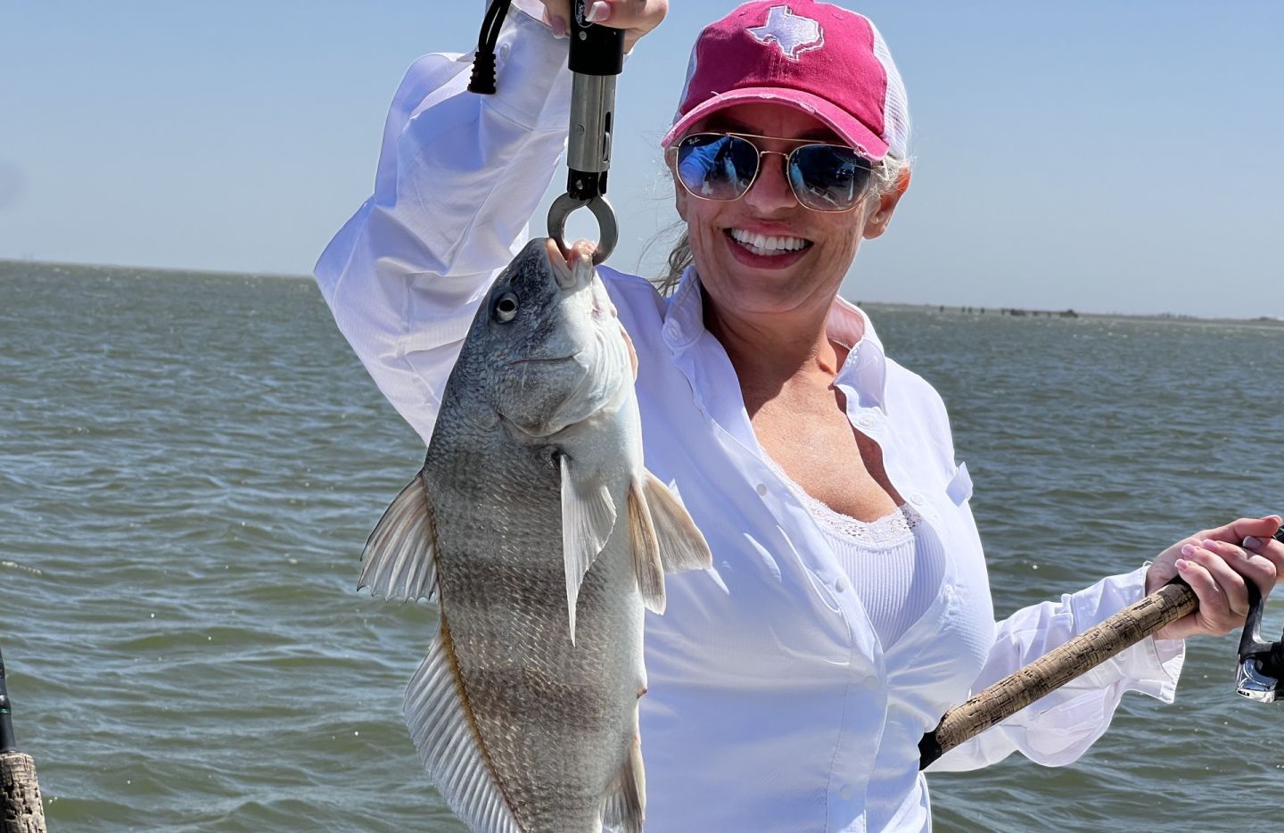 Black drum fish caught while fishing, held up with fishing pliers over water
