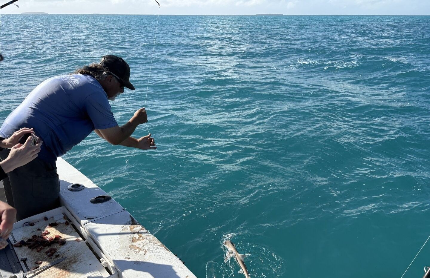 Fishing from boat deck with fish being reeled in from clear blue ocean water