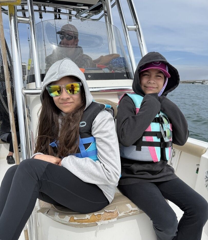 Two people sitting on a fishing boat wearing life jackets on the water