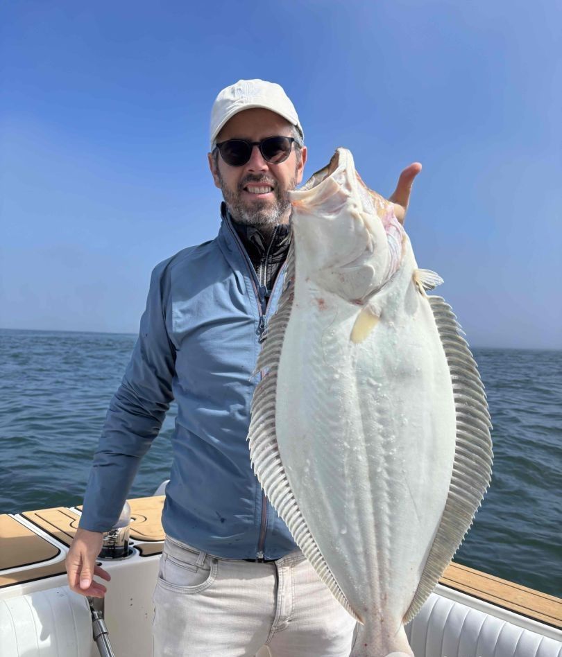 Angler displaying large California flounder catch on boat deck during ocean fishing trip