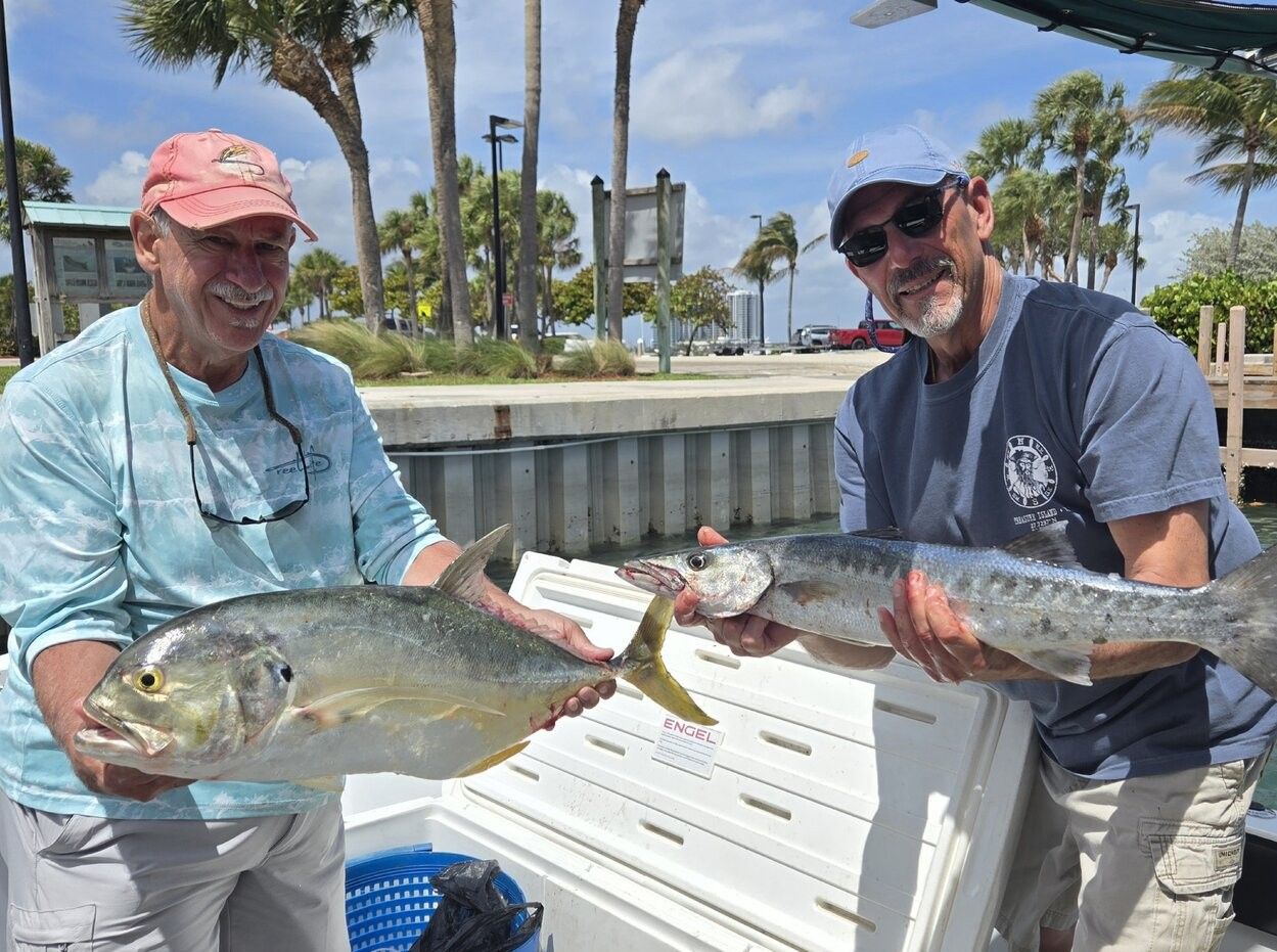 Two anglers displaying their catch of Crevalle Jack and Great Barracuda on fishing boat dock with palm trees in background
