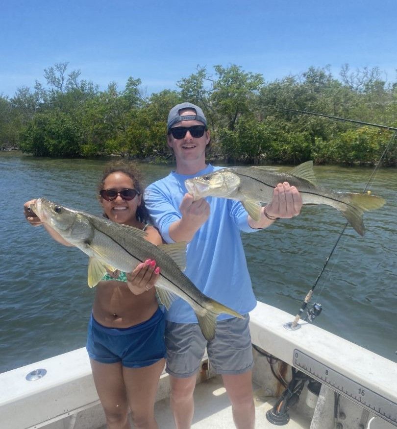 Two anglers displaying freshly caught snook on fishing boat with mangroves in background