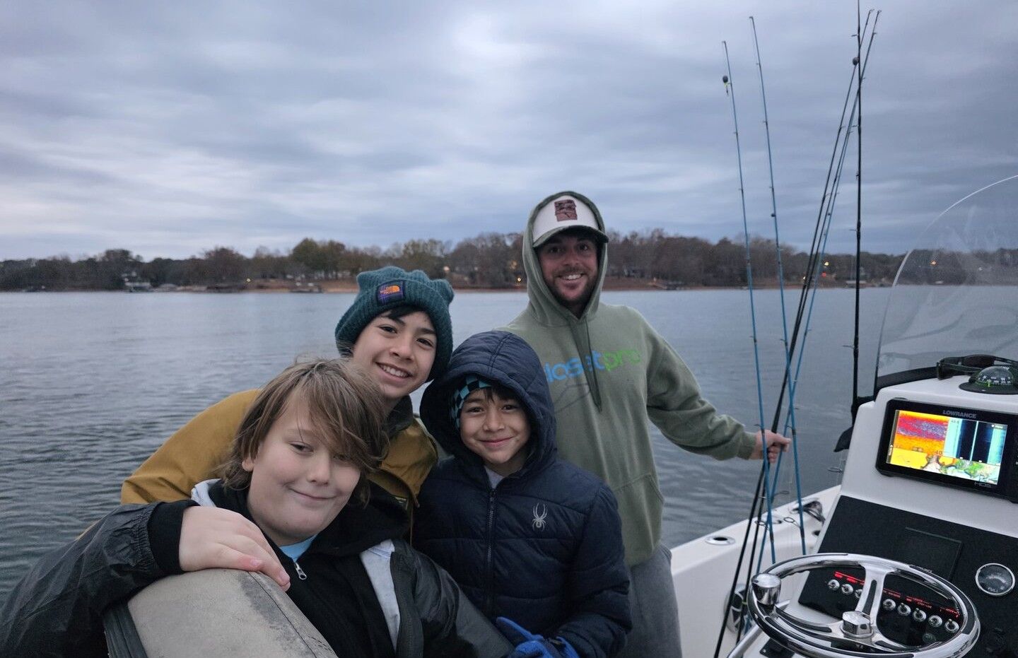 Four people posing together on a fishing boat with rods and fish finder equipment visible