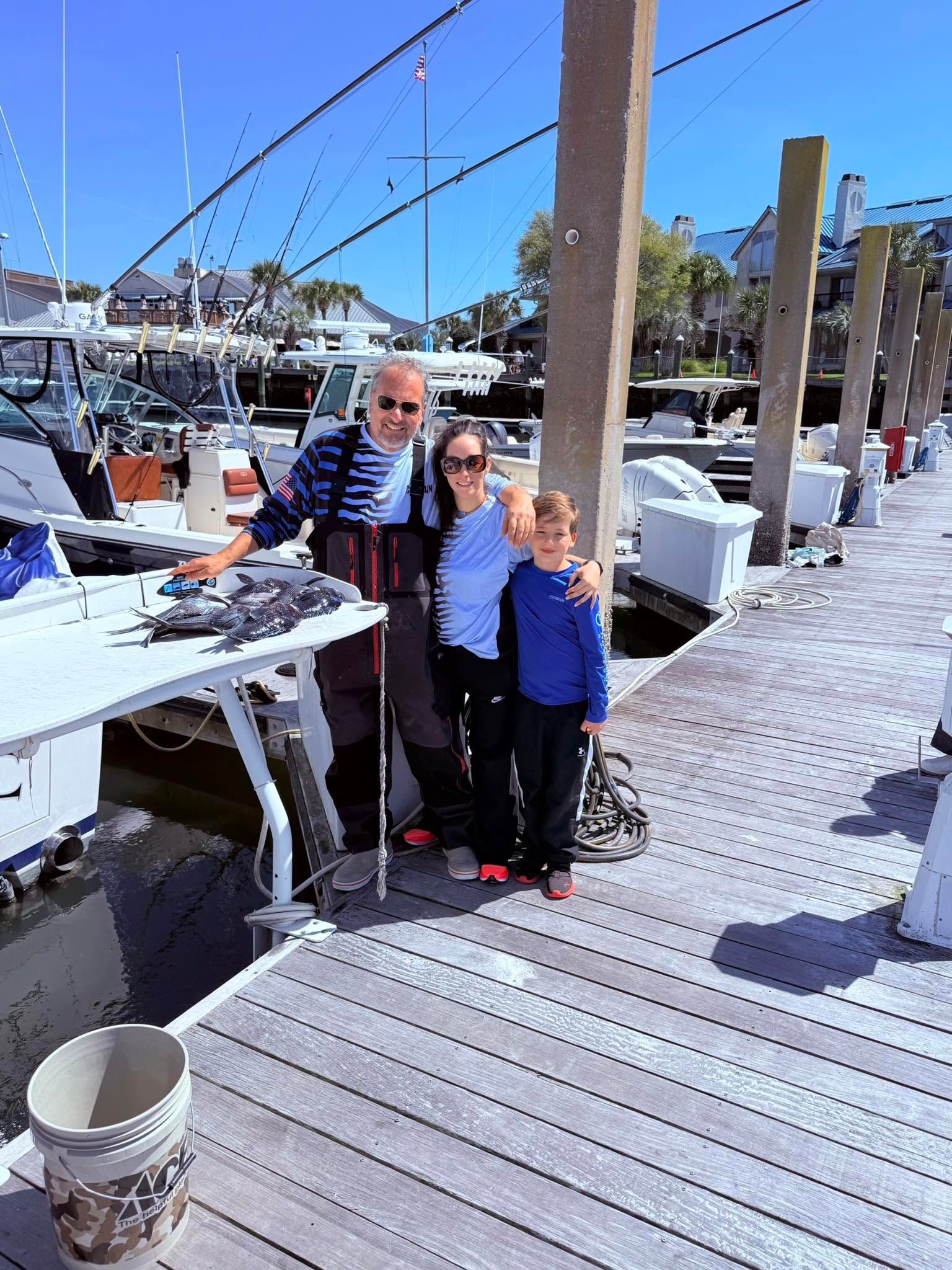 Family posing on wooden dock at marina with fresh caught fish displayed on cleaning table