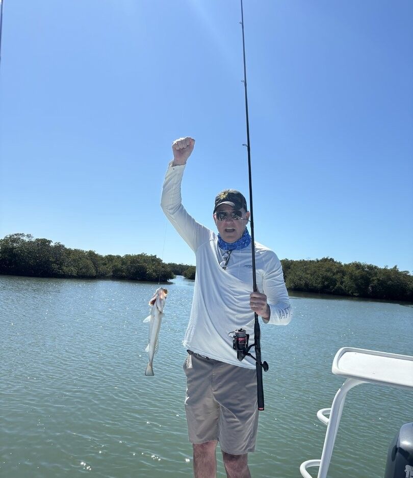 Angler celebrating with caught fish and fishing rod on boat in calm waters