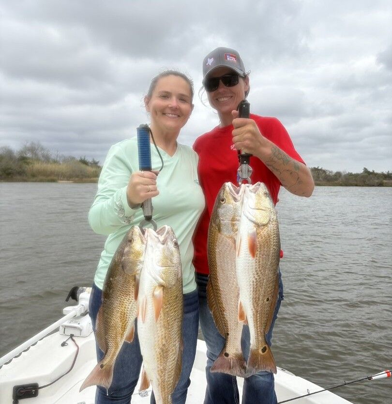 Two anglers displaying four freshly caught redfish on boat deck
