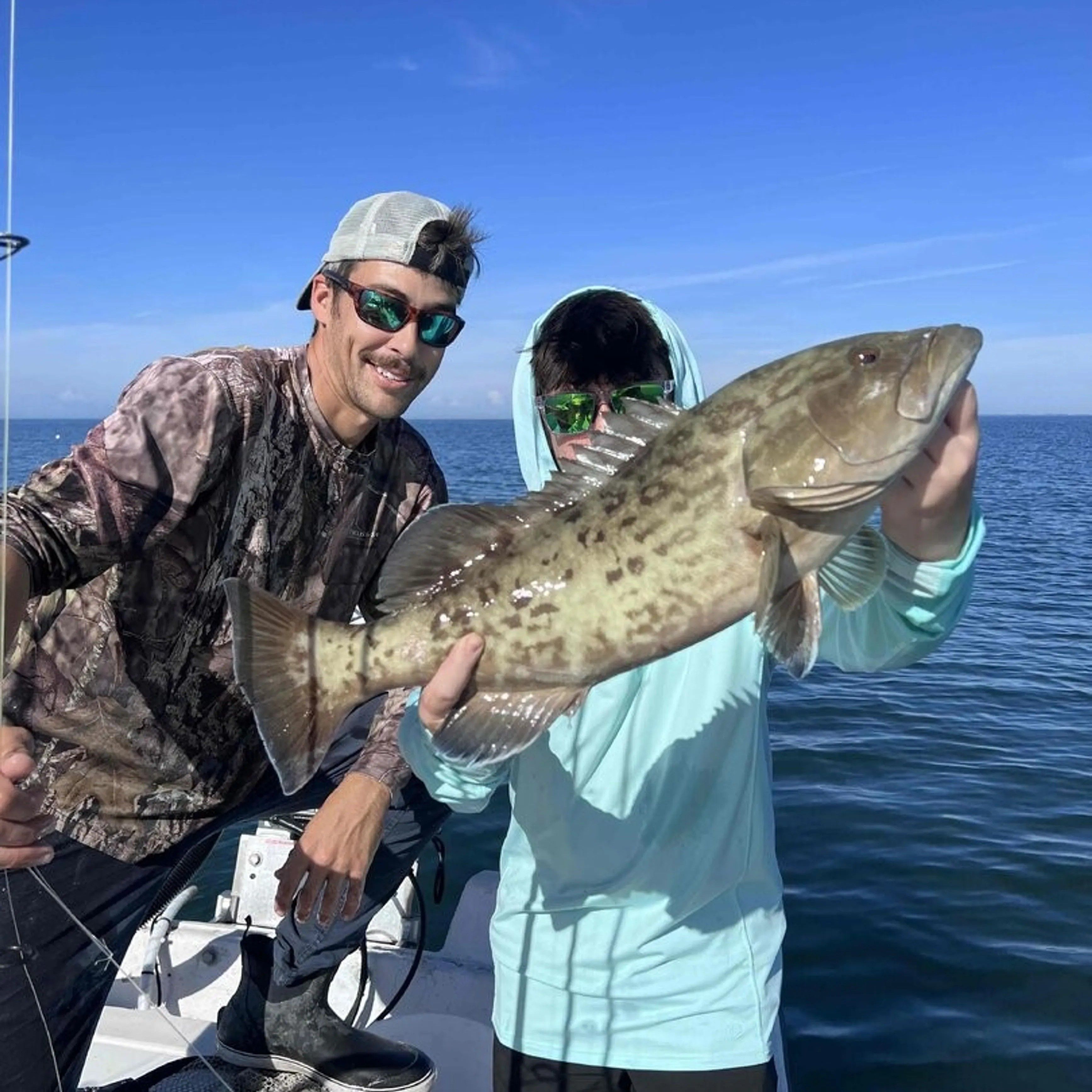 Two anglers holding a large gag grouper caught while fishing on the ocean