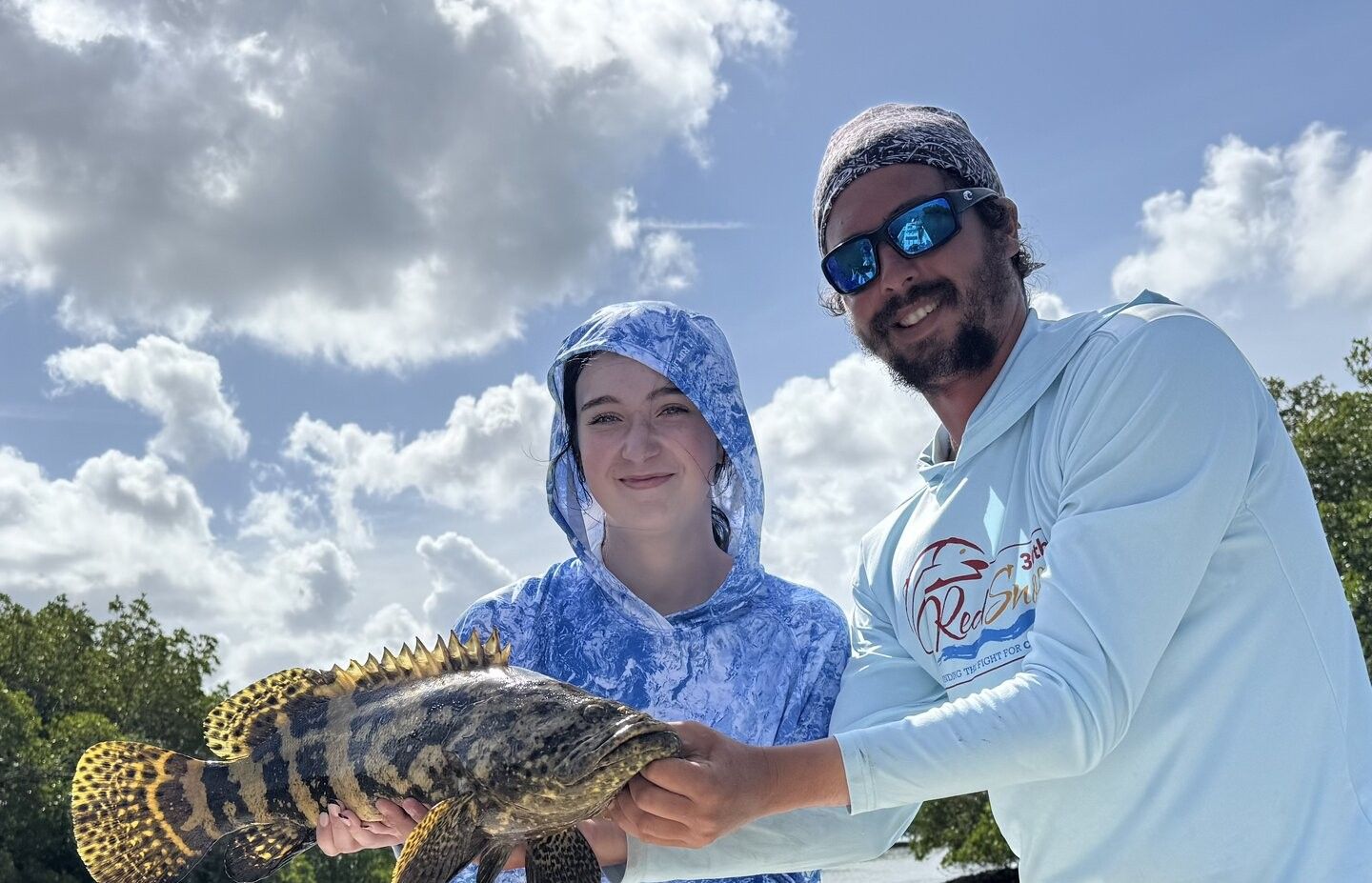Two people holding a freshly caught Goliath Grouper during a fishing trip