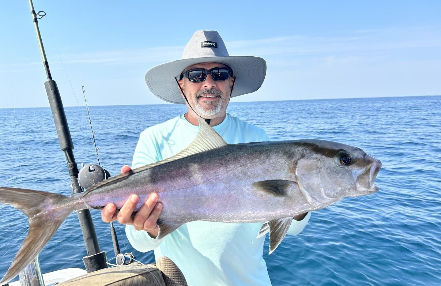 Angler holding a large Greater Amberjack fish on boat deck over ocean water