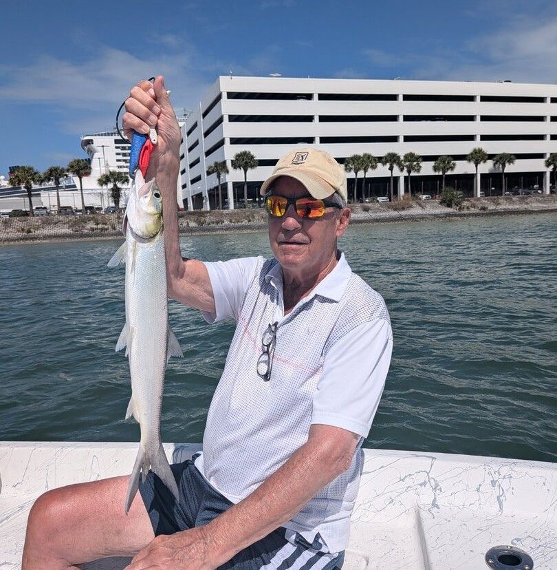 Angler holding caught ladyfish on fishing boat with waterfront buildings in background