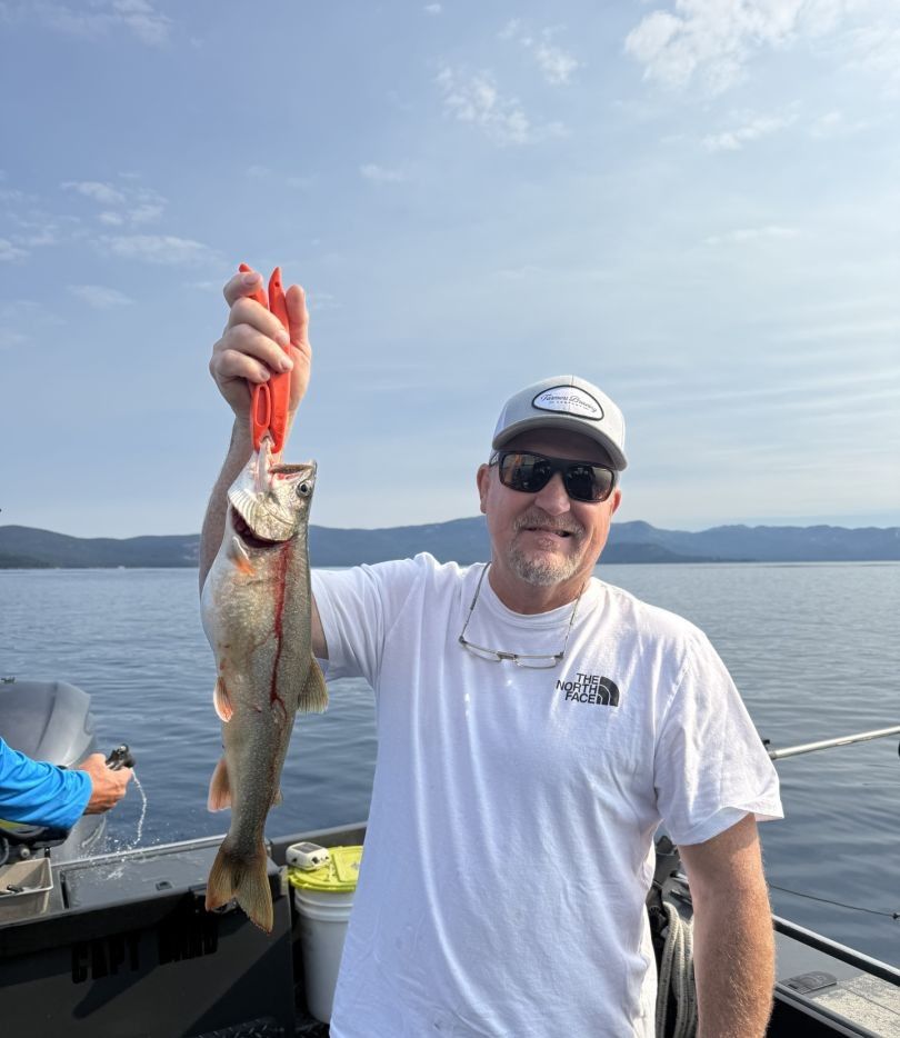Lake trout caught while fishing, being held up on a boat with mountains in the background