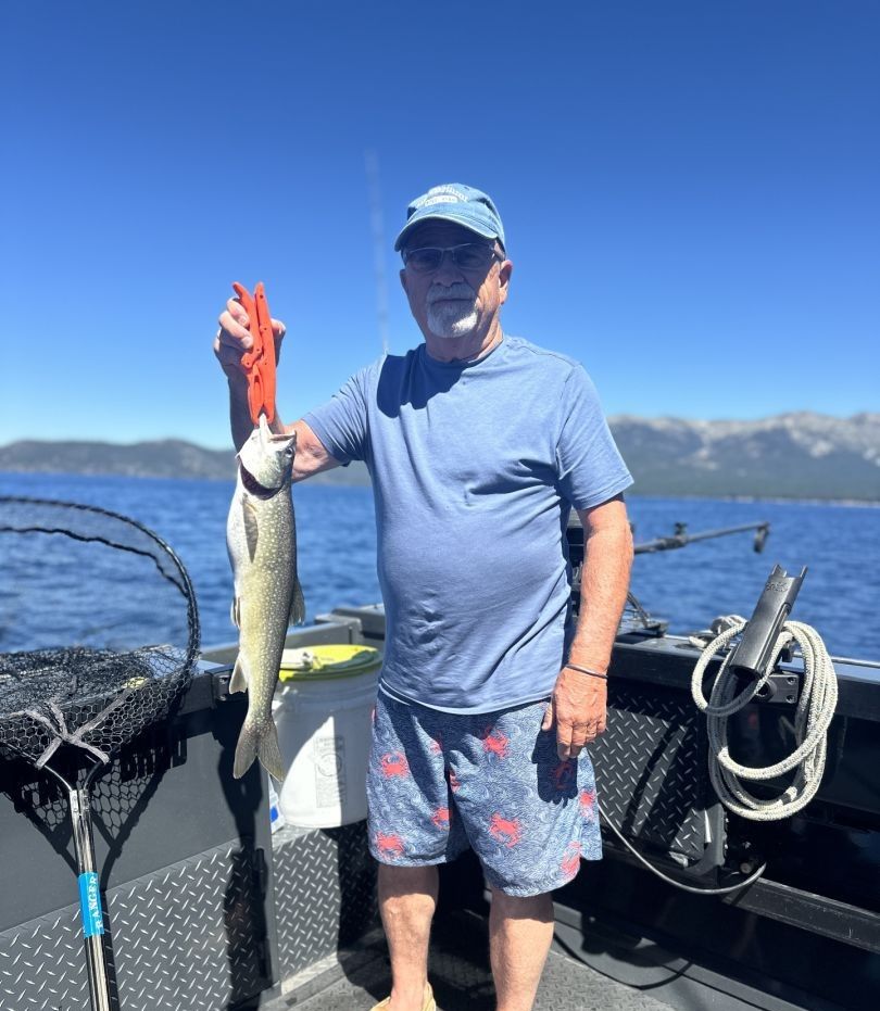 Angler holding freshly caught lake trout on fishing boat with mountains in background