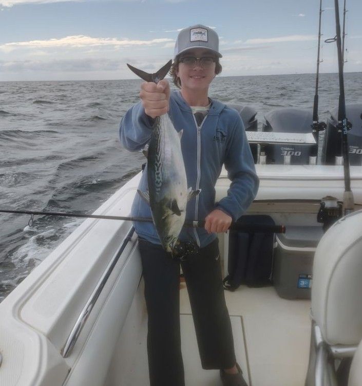 Angler holding freshly caught little tunny on fishing boat deck at sea
