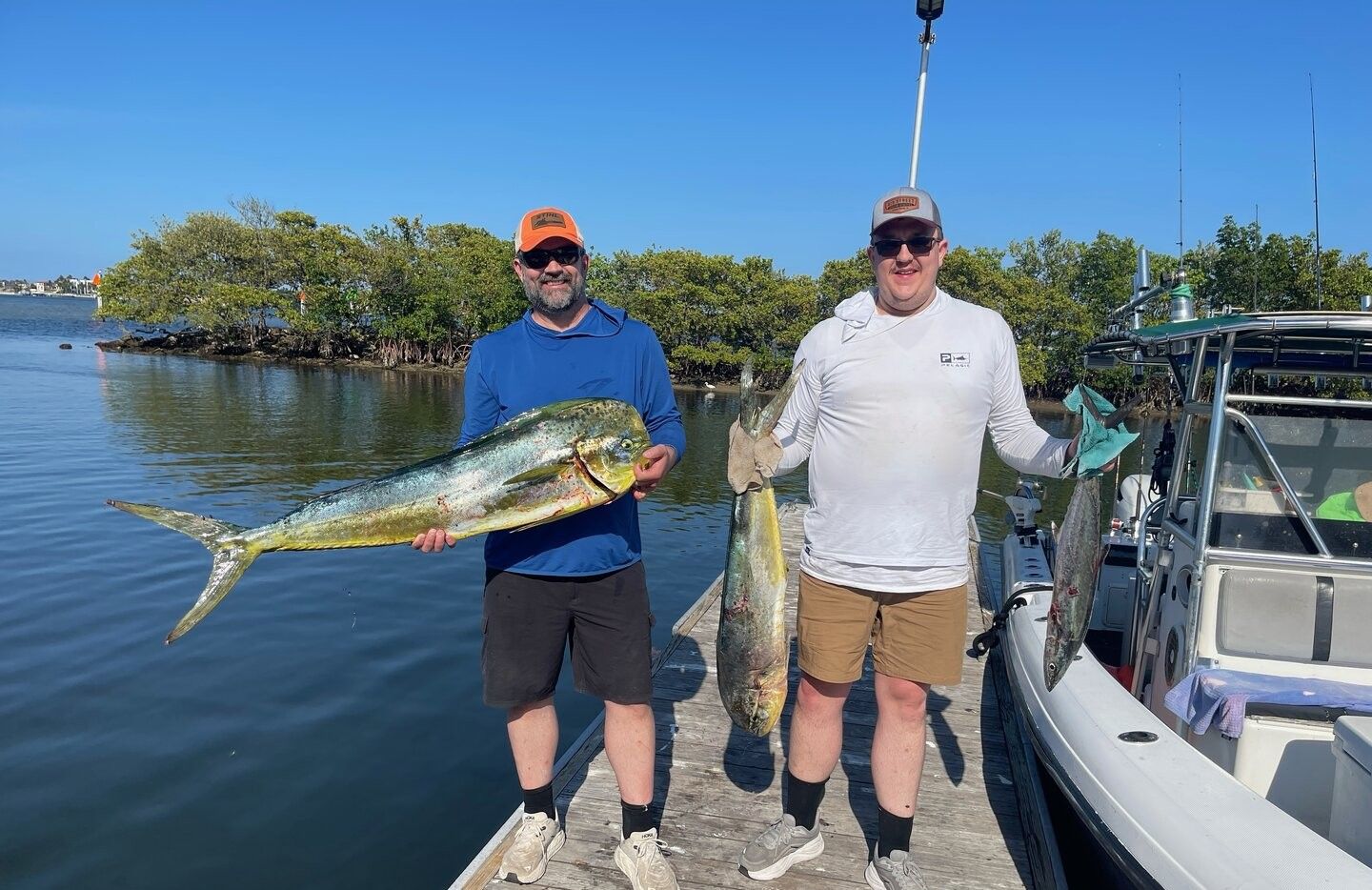 Two anglers displaying freshly caught mahi mahi and king mackerel on fishing boat dock