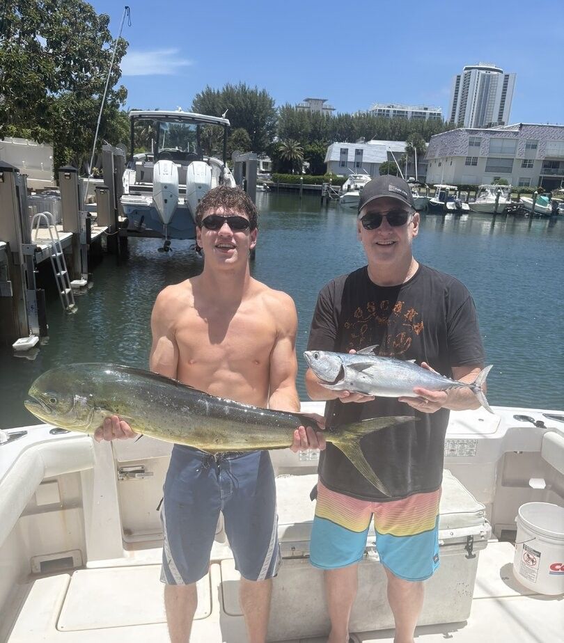 Two anglers displaying fresh caught mahi mahi and little tunny fish on boat deck at marina