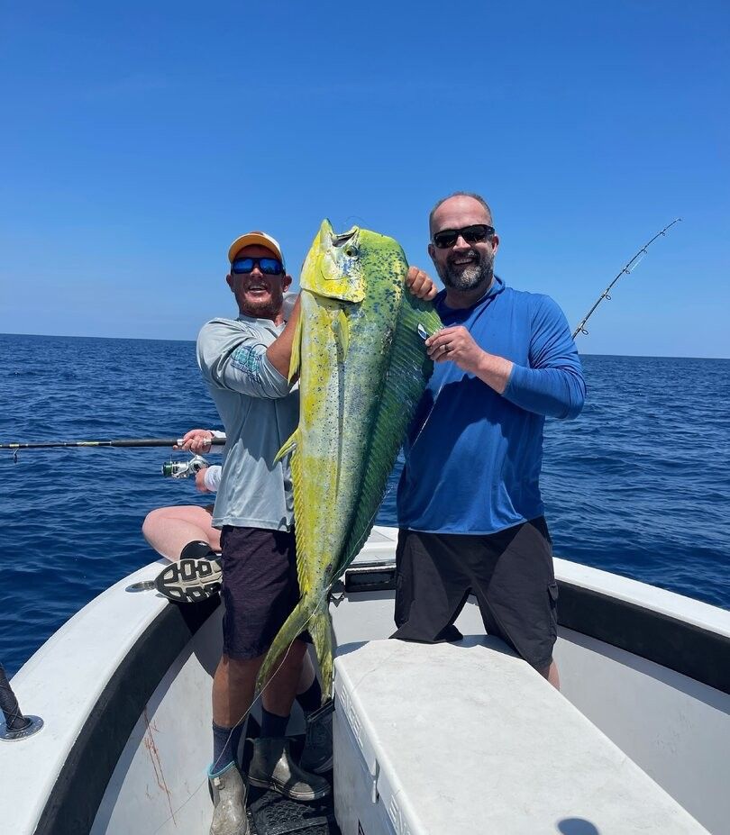 Two anglers holding a large mahi mahi on a fishing boat in open ocean waters