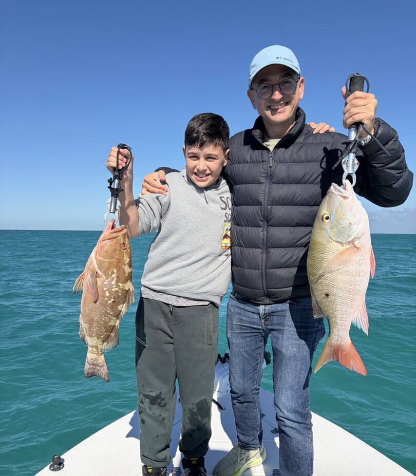 Two anglers displaying their catch of mutton snapper and red grouper on boat deck with ocean background