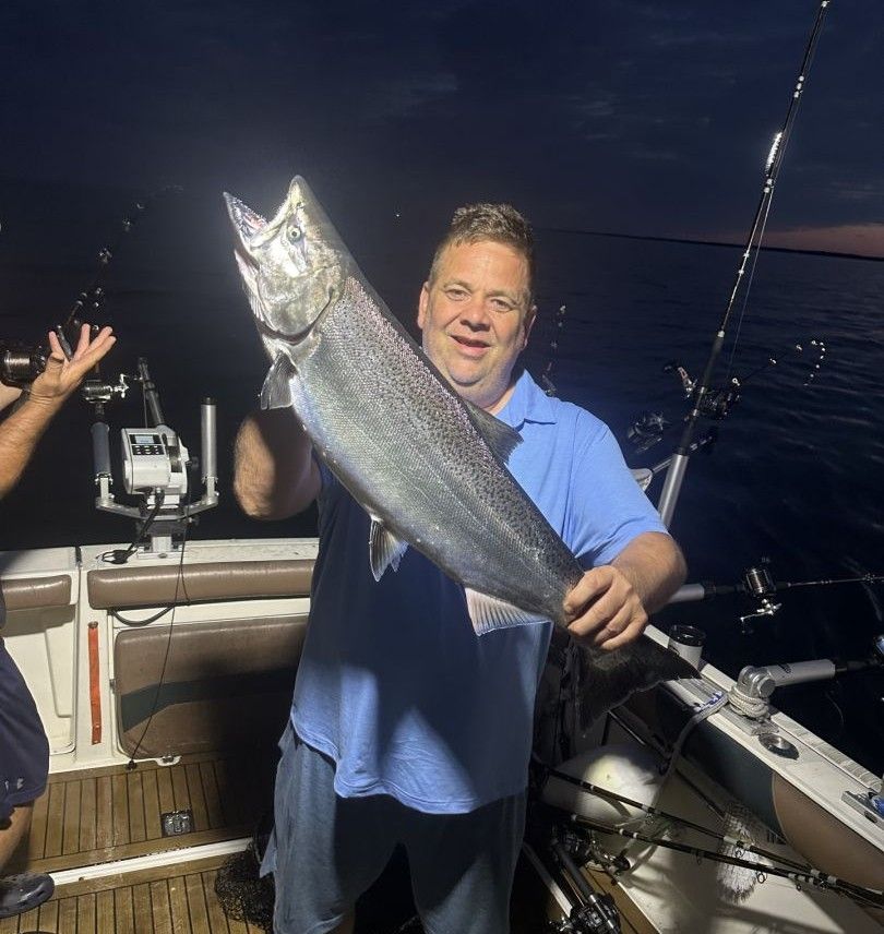 Angler holding large Chinook salmon on fishing boat at night