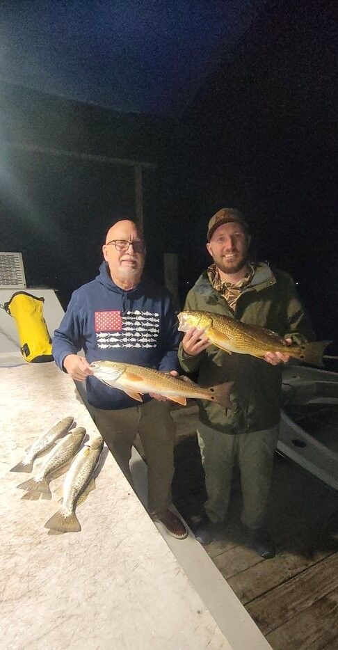 Two anglers displaying freshly caught redfish on boat deck at night