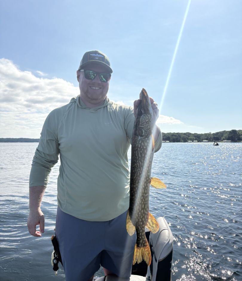 Angler holding a large Northern Pike on a boat during a successful fishing trip