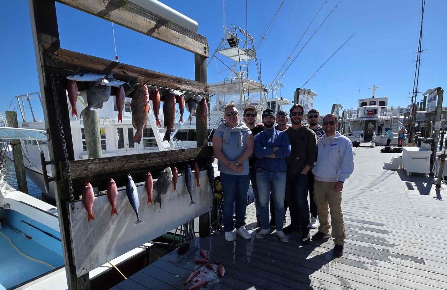 Fishing charter group displaying their catch of red grouper and other fish on marina dock with boats in background