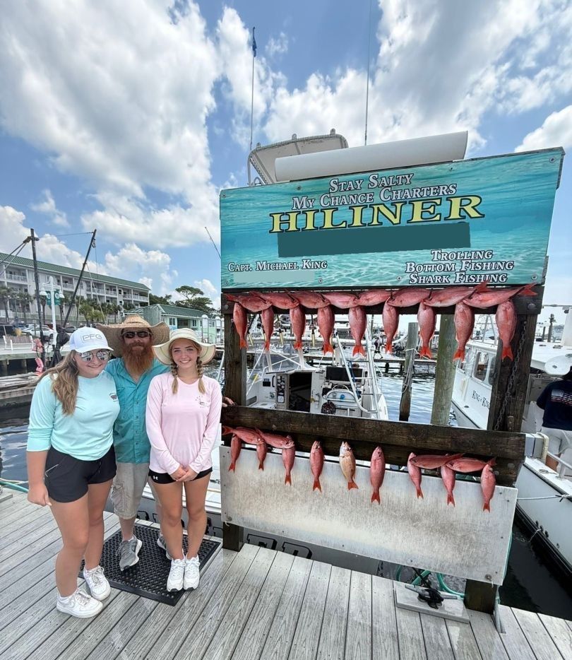 Charter fishing display board showing red snapper catch on marina dock with boats in background