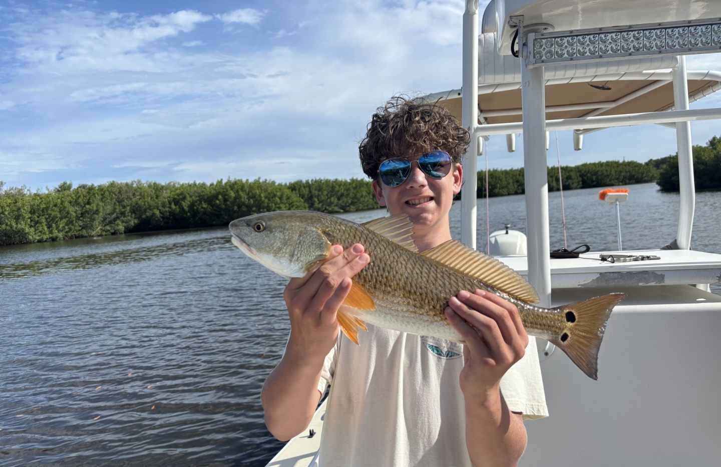 Angler holding freshly caught redfish on fishing boat in coastal waters with mangroves in background
