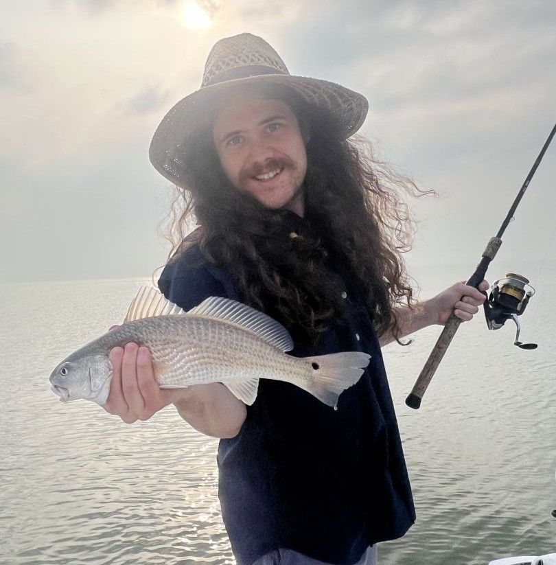 Angler holding freshly caught redfish with fishing rod by water