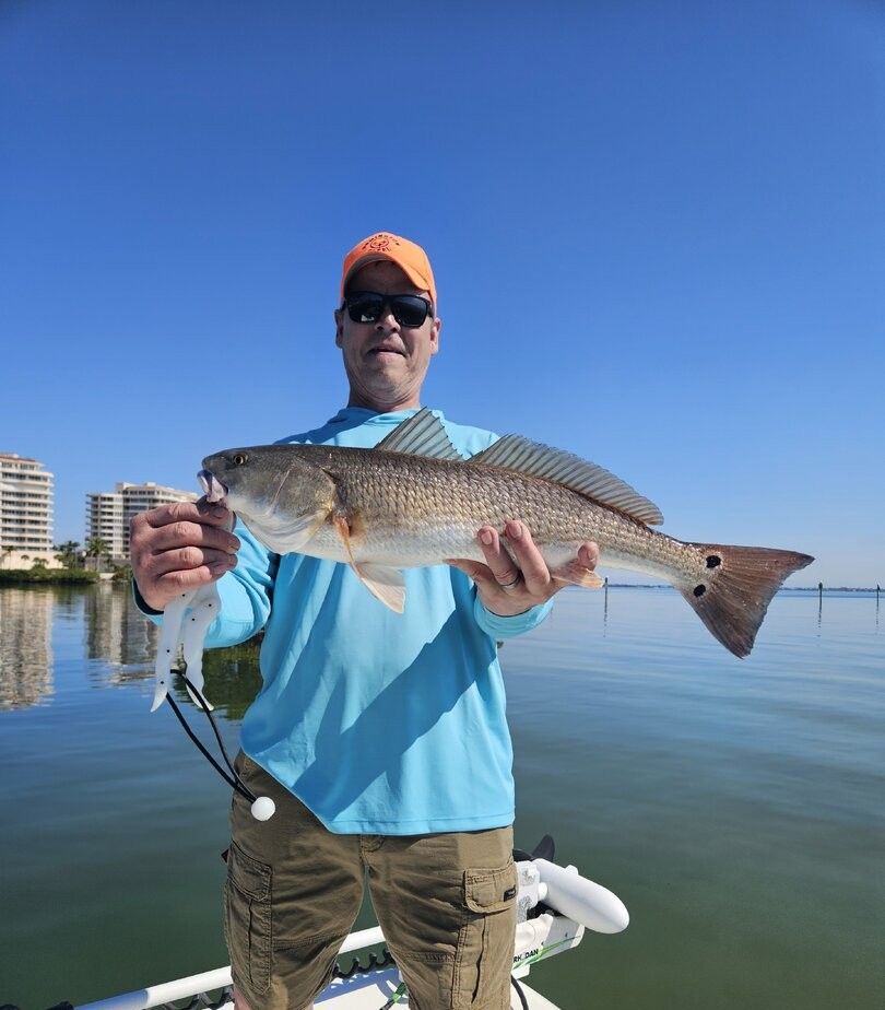 Angler holding caught redfish on boat with calm water and buildings in background