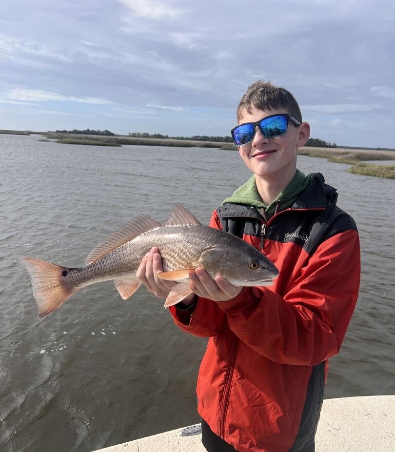 Angler holding caught redfish on boat in coastal waters