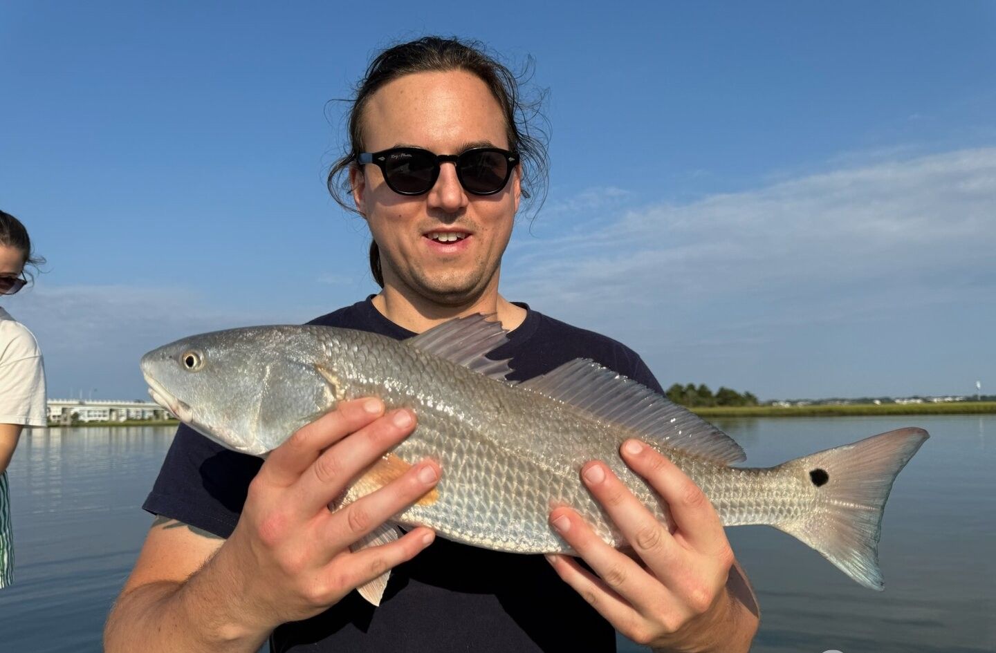 Angler holding freshly caught redfish on fishing boat with water and shoreline in background