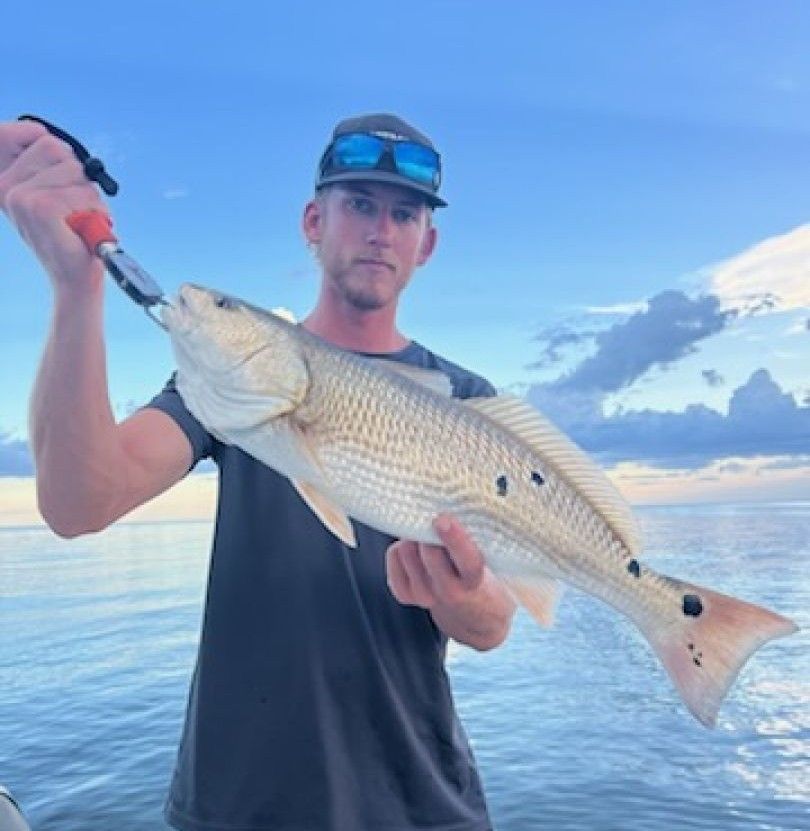 Angler holding caught redfish on fishing boat with ocean and mountains in background