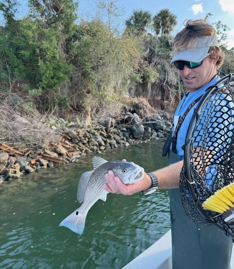 Angler holding caught redfish over water from boat