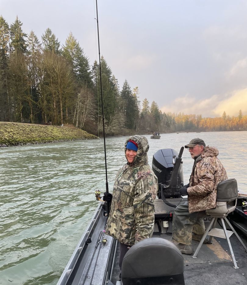 Two anglers fishing from a boat on a river with forested shoreline