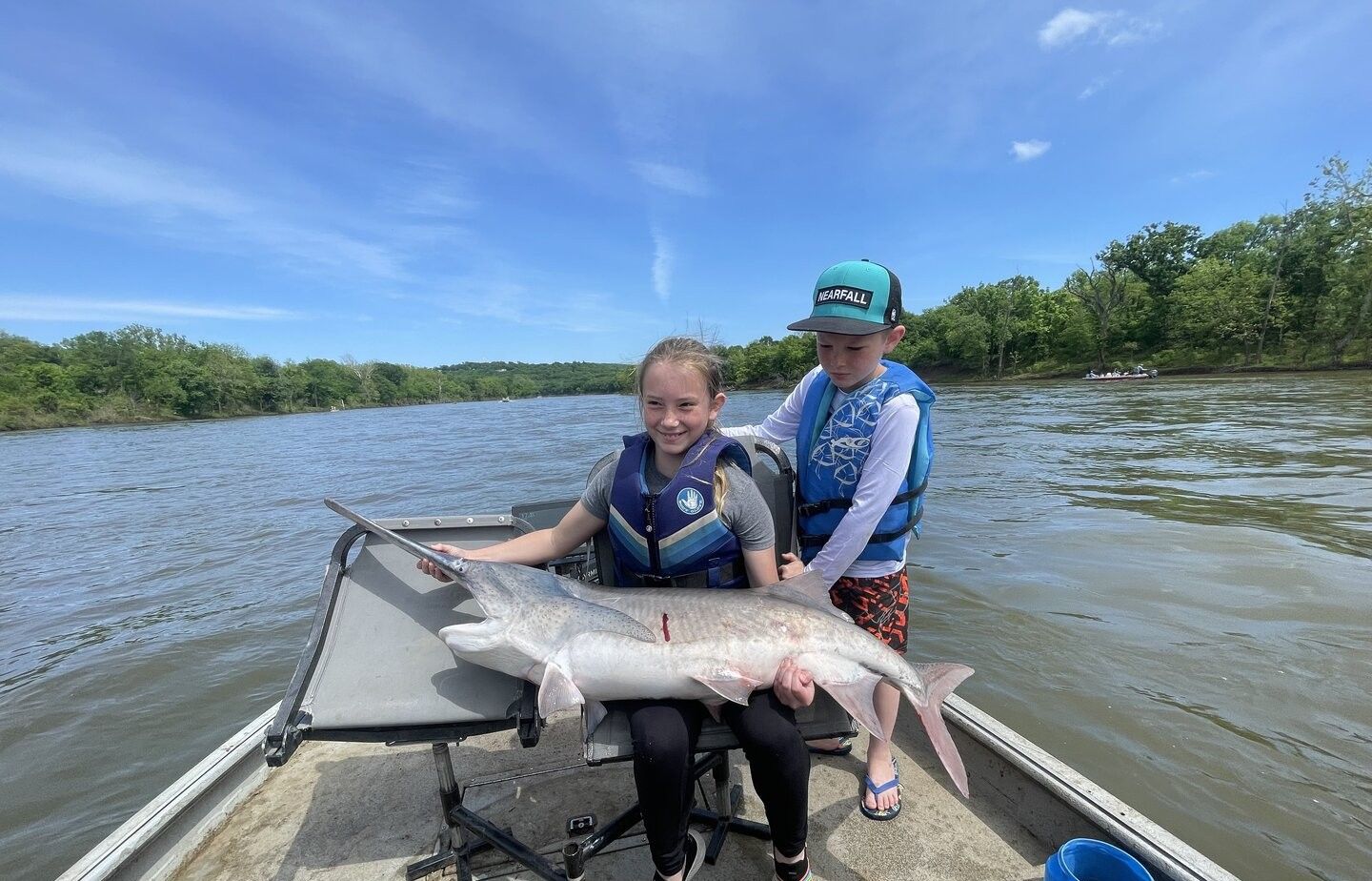 Large fish caught during fishing trip on river with boat and wooded shoreline