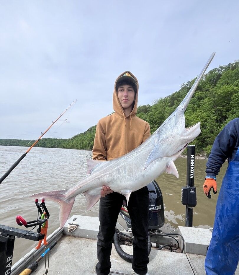 Large silver fish being held on fishing boat with rod and motor visible