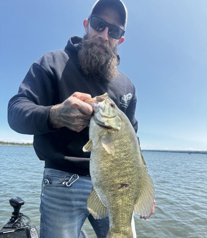 Angler holding caught smallmouth bass on lake during fishing trip