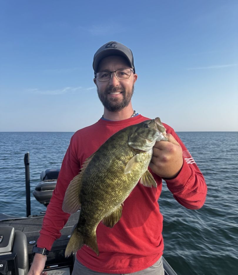Angler holding caught smallmouth bass on boat in open water