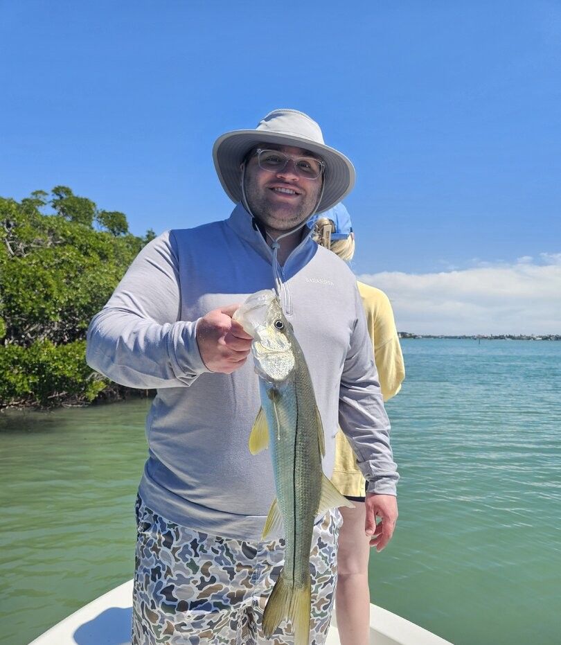 Freshly caught snook held up on fishing boat in tropical waters with mangroves in background