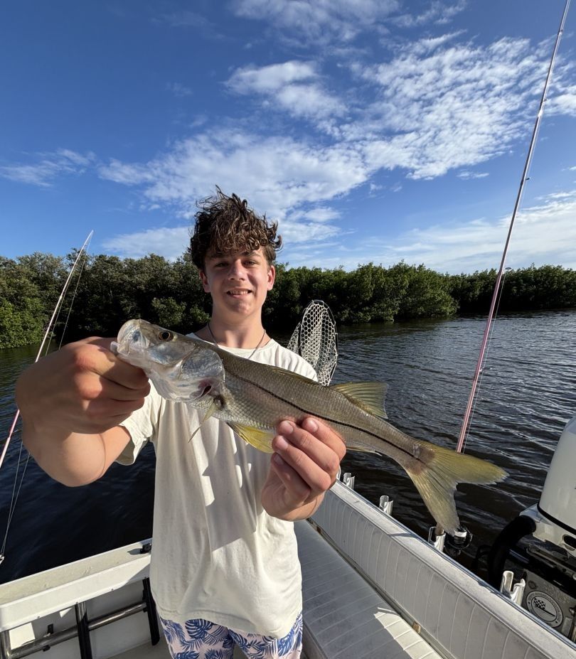 Angler holding freshly caught snook on fishing boat with river and mangroves in background