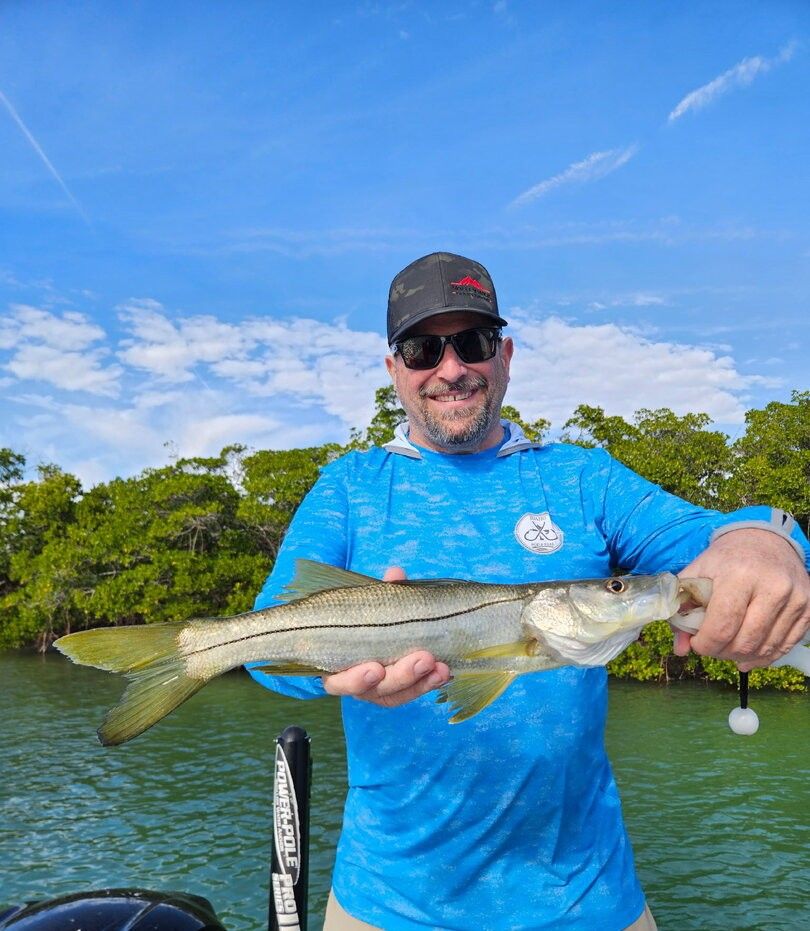 Angler holding freshly caught snook on fishing boat with mangroves in background
