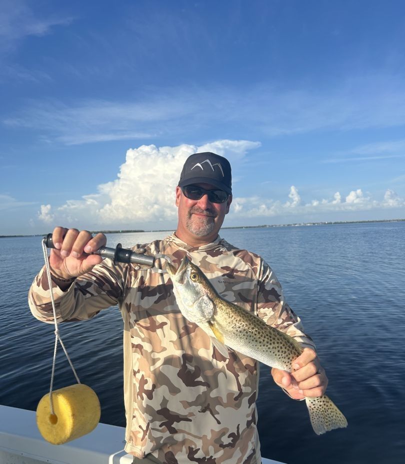 Freshly caught speckled trout being held up on fishing boat with ocean waters in background