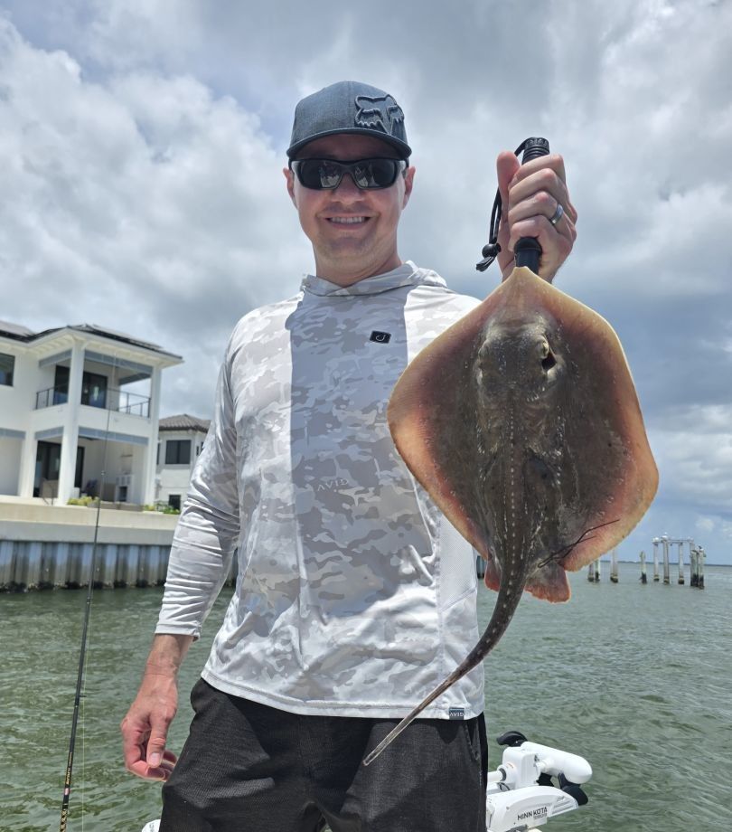 Angler holding caught stingray on fishing boat in coastal waters