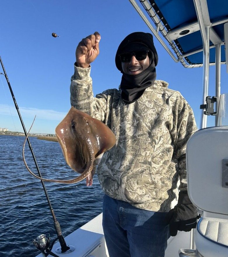 Fishing boat deck with caught stingray being held up on sunny day