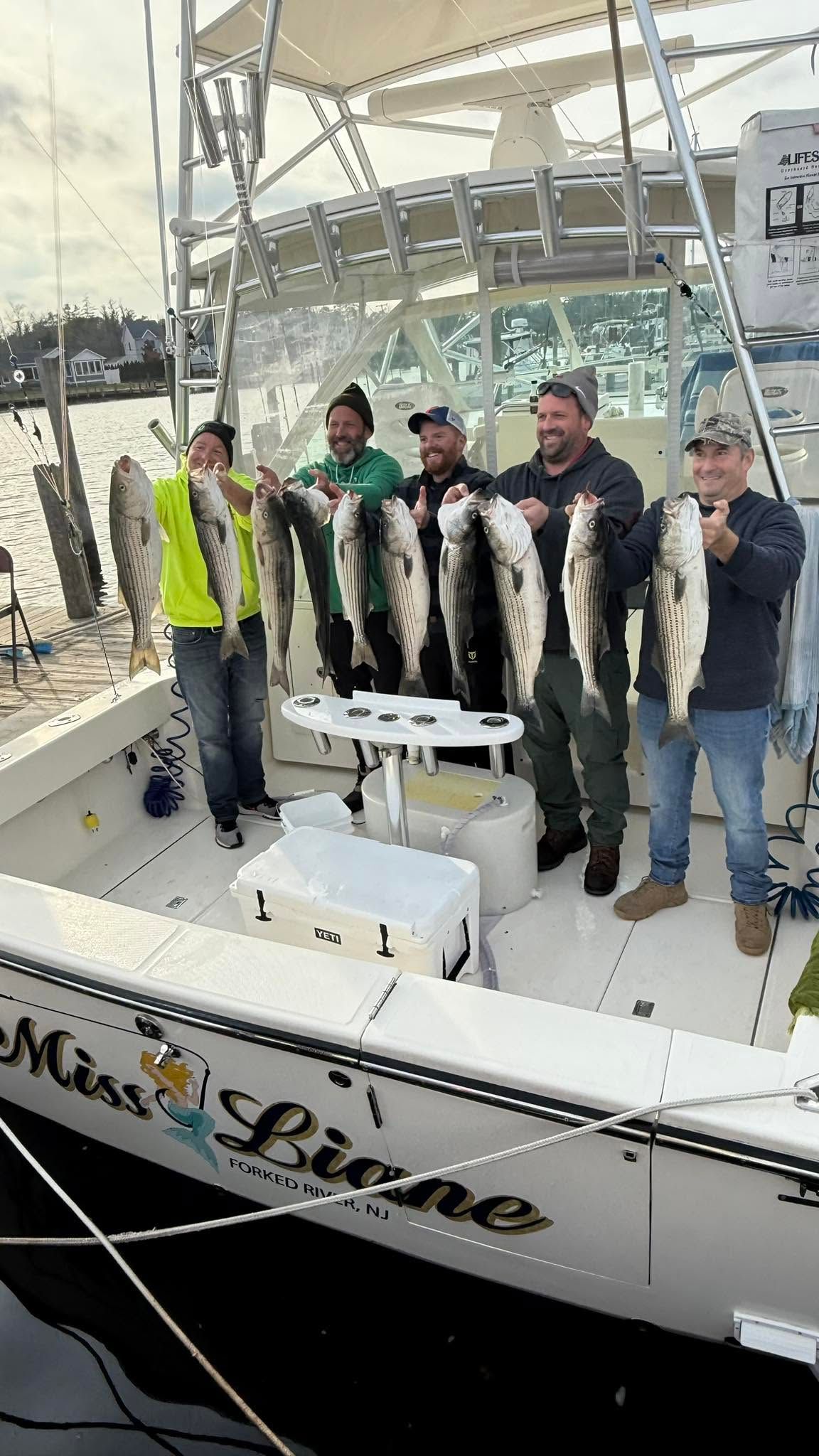 Group of anglers displaying their catch of striped bass on fishing boat deck